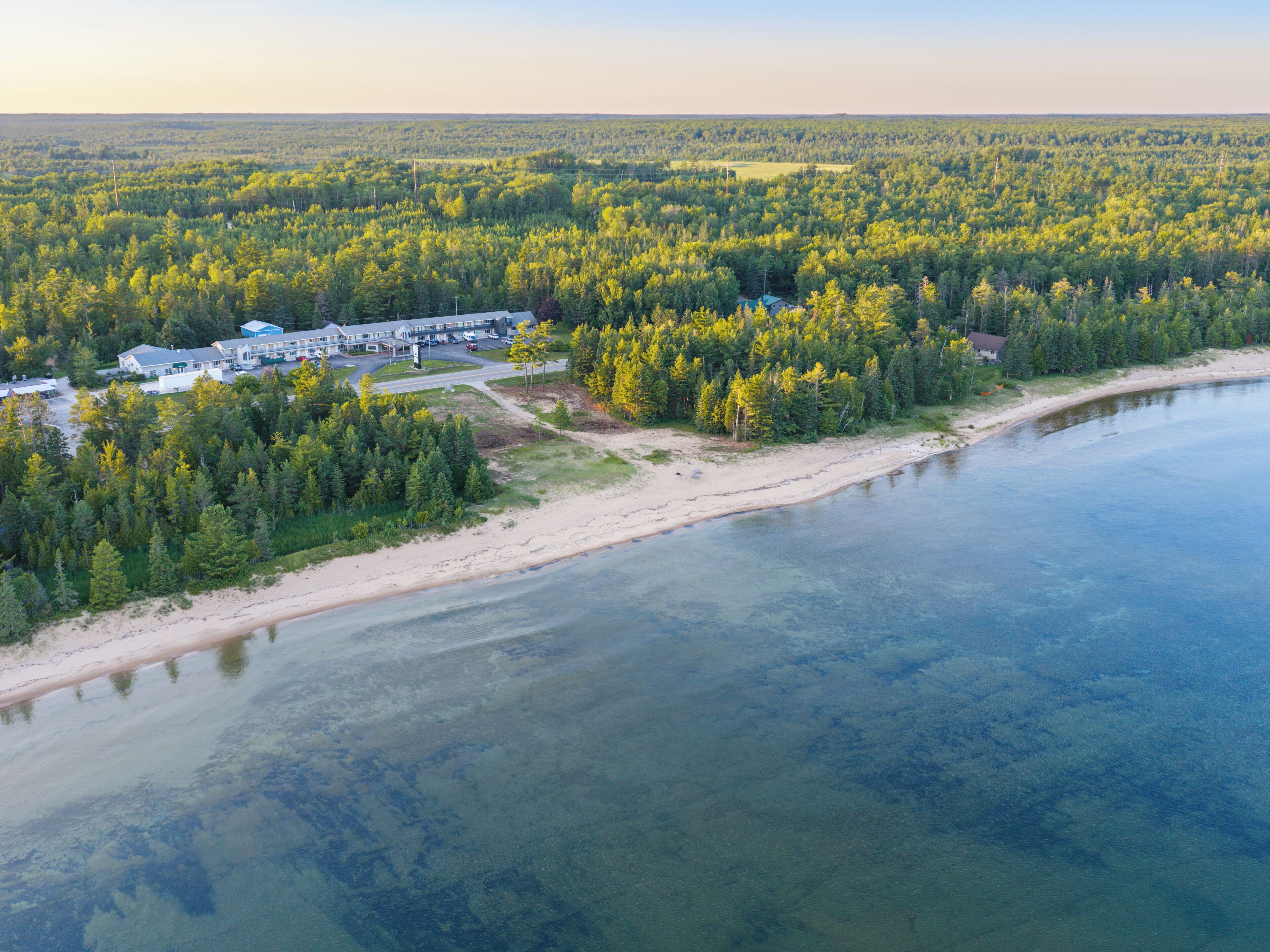 An aerial view of a coastal area with a beach, forested land, and a building complex.