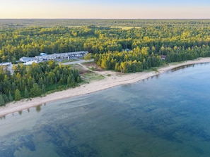 An aerial view of a coastal area with a beach, forested land, and a building complex. - Manistique Sands (Manistique)