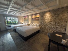Habitación de hotel con dos camas, una pared de acento de piedra, un ventanal con vistas y una mesa con una taza.