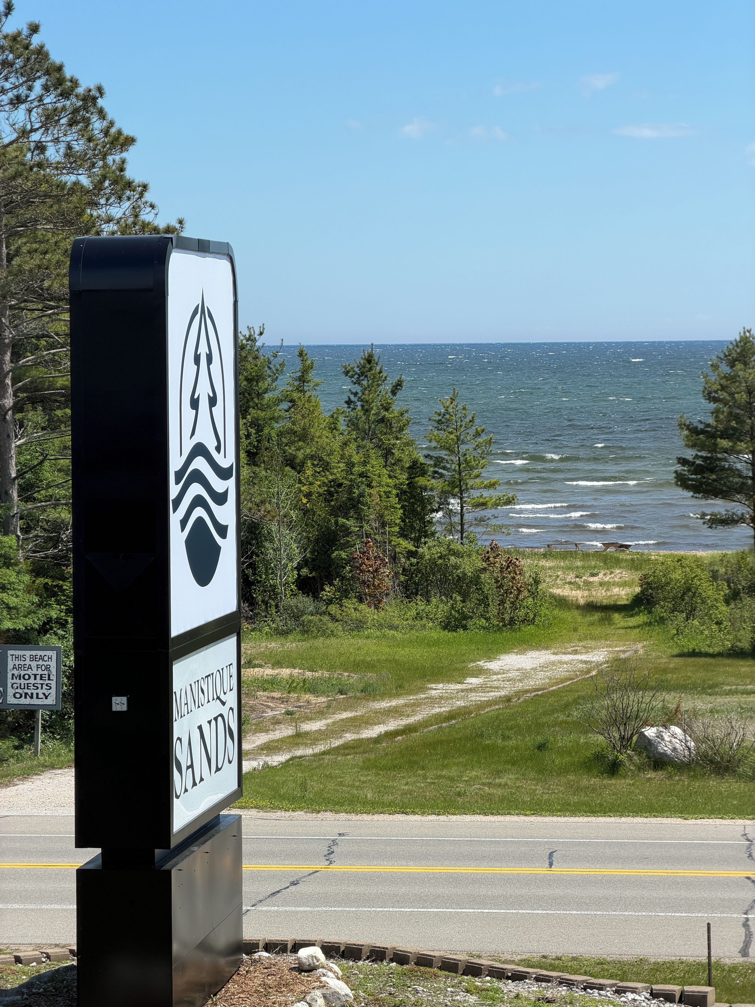 A beach sign with a logo and text indicating 'Manistique Sands' and a beach area for motel guests only.