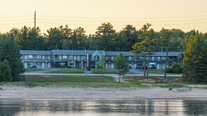 Un motel con aparcamiento, una pequeña zona de playa y una masa de agua al frente.