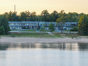 A motel with a parking lot, a small beach area, and a body of water in the foreground. - Manistique Sands (Manistique)