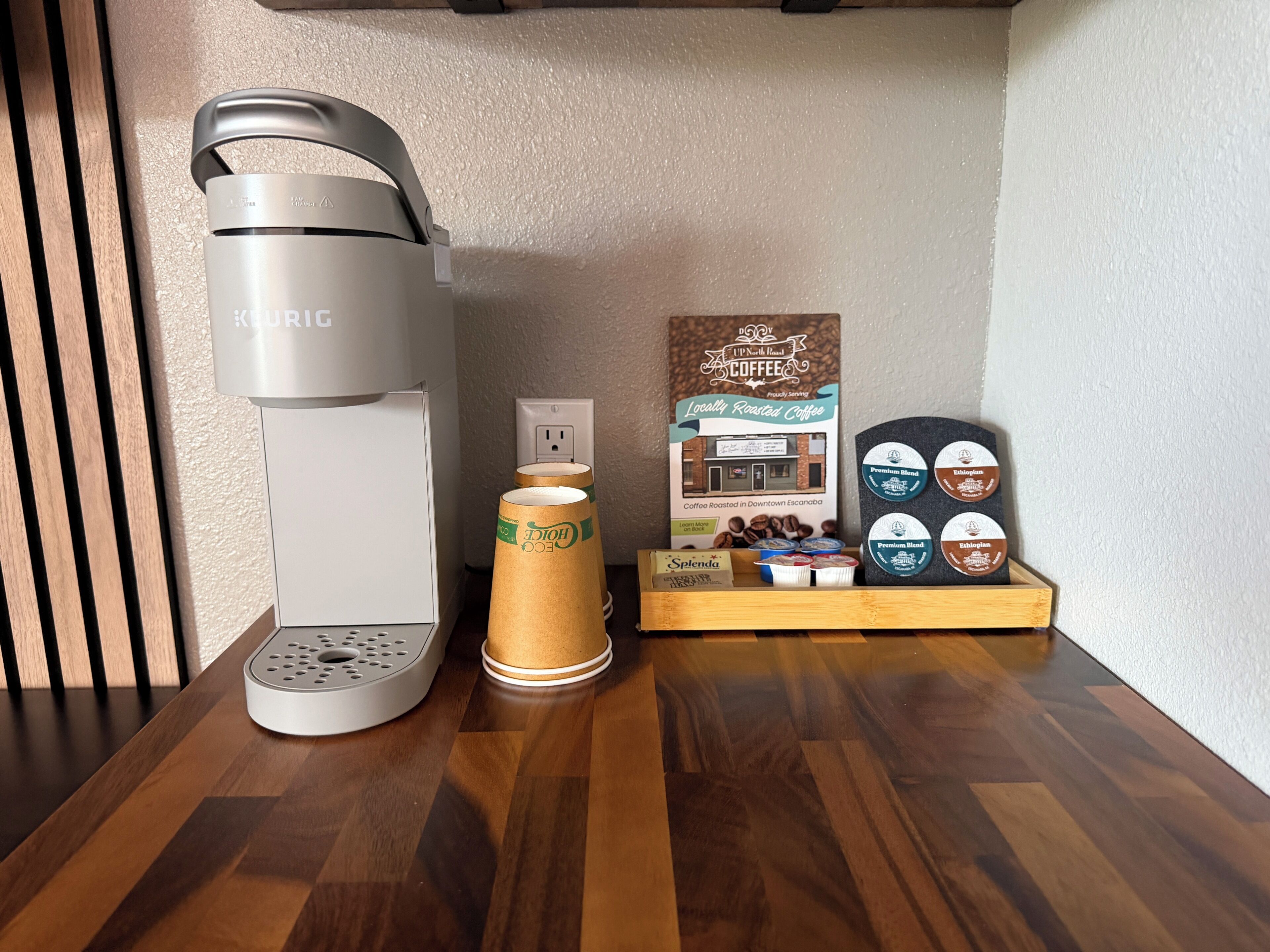 A coffee maker, a coffee grinder, and a display of coffee beans and pods on a wooden table.