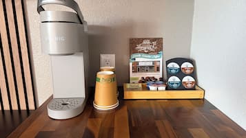 Uma cafeteira, um moedor de café, e uma seleção de grãos e cápsulas de café sobre uma mesa de madeira.