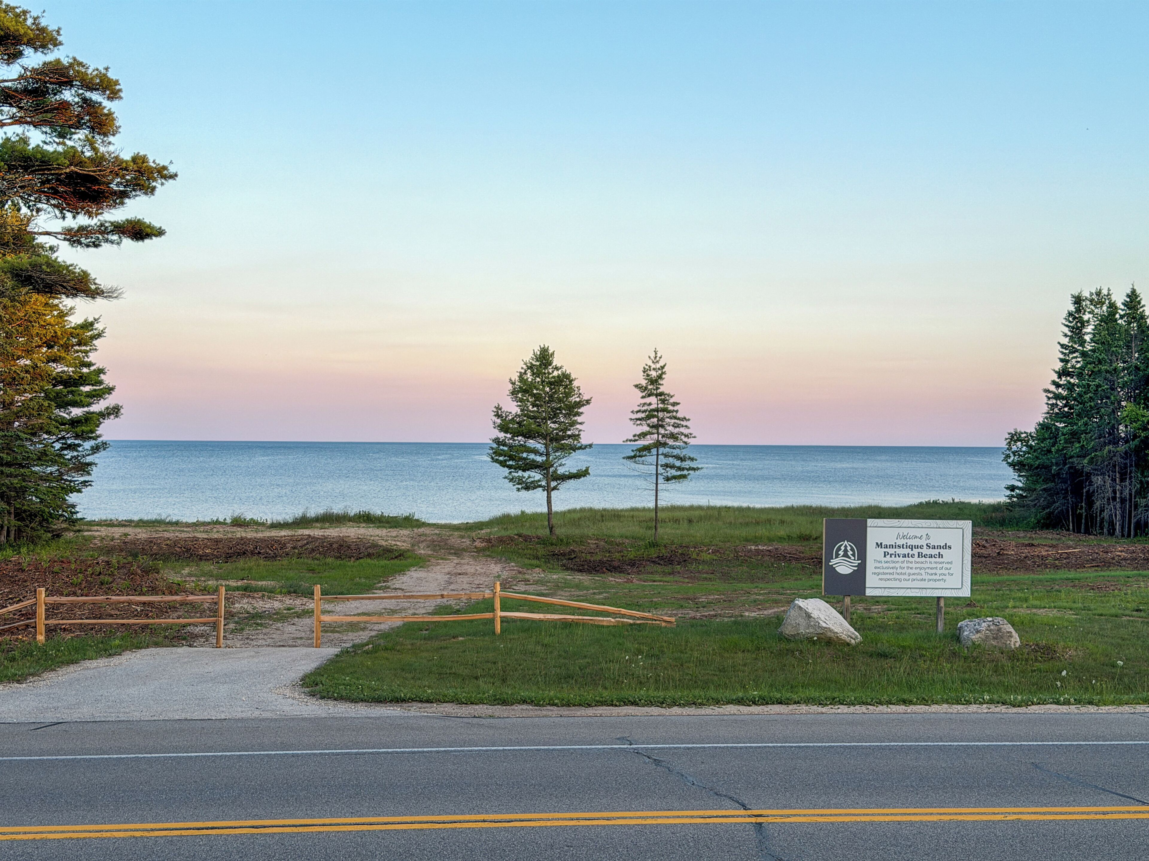 A beach entrance with a sign, a pathway, and a view of the ocean.