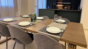 Un comedor con una larga mesa de madera dispuesta para cuatro personas, sillas tapizadas en gris y lámparas colgantes.