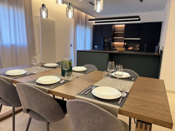 A dining area with a long wooden table set for four, grey upholstered chairs, and hanging pendant lights. - Elegant Apartment in the Center of Palermo, Notarbartolo Design Apartment (Palermo)