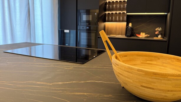 Una cocina moderna con una encimera oscura, un cuenco de madera y una botellera de vidrio.