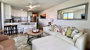 Ein modernes Wohnzimmer mit einem weißen Sofa, einem Couchtisch und einer Küchenzeile mit weißen Schränken und einem Esstisch.
