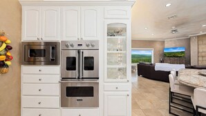 A kitchen with built-in appliances, a dining area with a round table, and a view of the outdoors. - La Cresta: Hill Country Retreat with Heatable Pool, Fitness Room & Views (Helotes)
