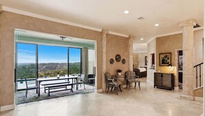 A spacious living area with a large window, a dining table, and two chairs. - La Cresta: Hill Country Retreat with Heatable Pool, Fitness Room & Views (Helotes)