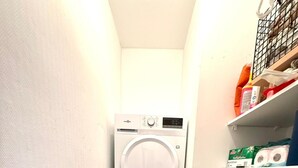 A laundry room with stacked washers and dryers, wooden flooring, and shelves with laundry supplies.