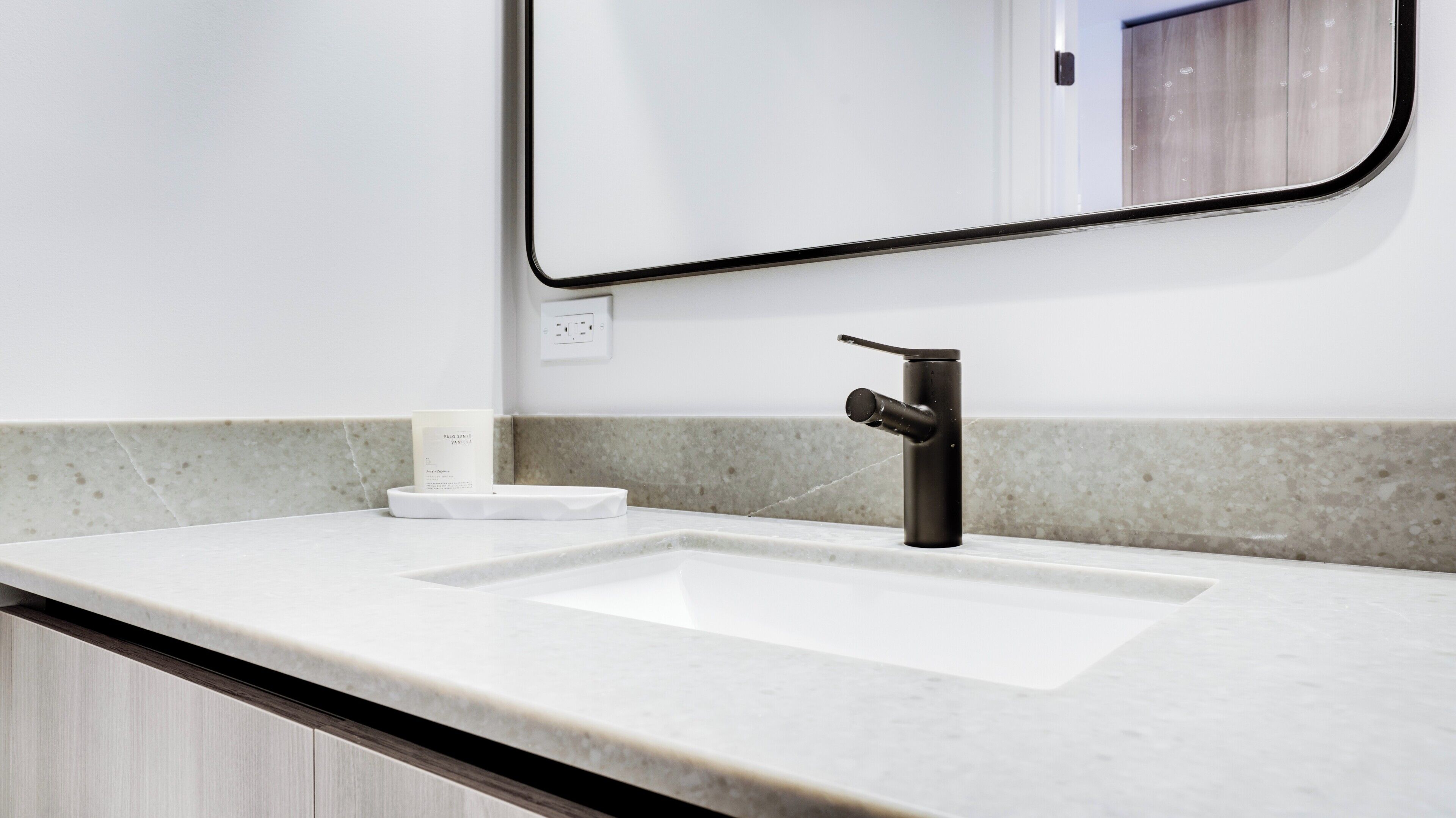 A bathroom with a white sink, a black faucet, and a mirror with a black frame.