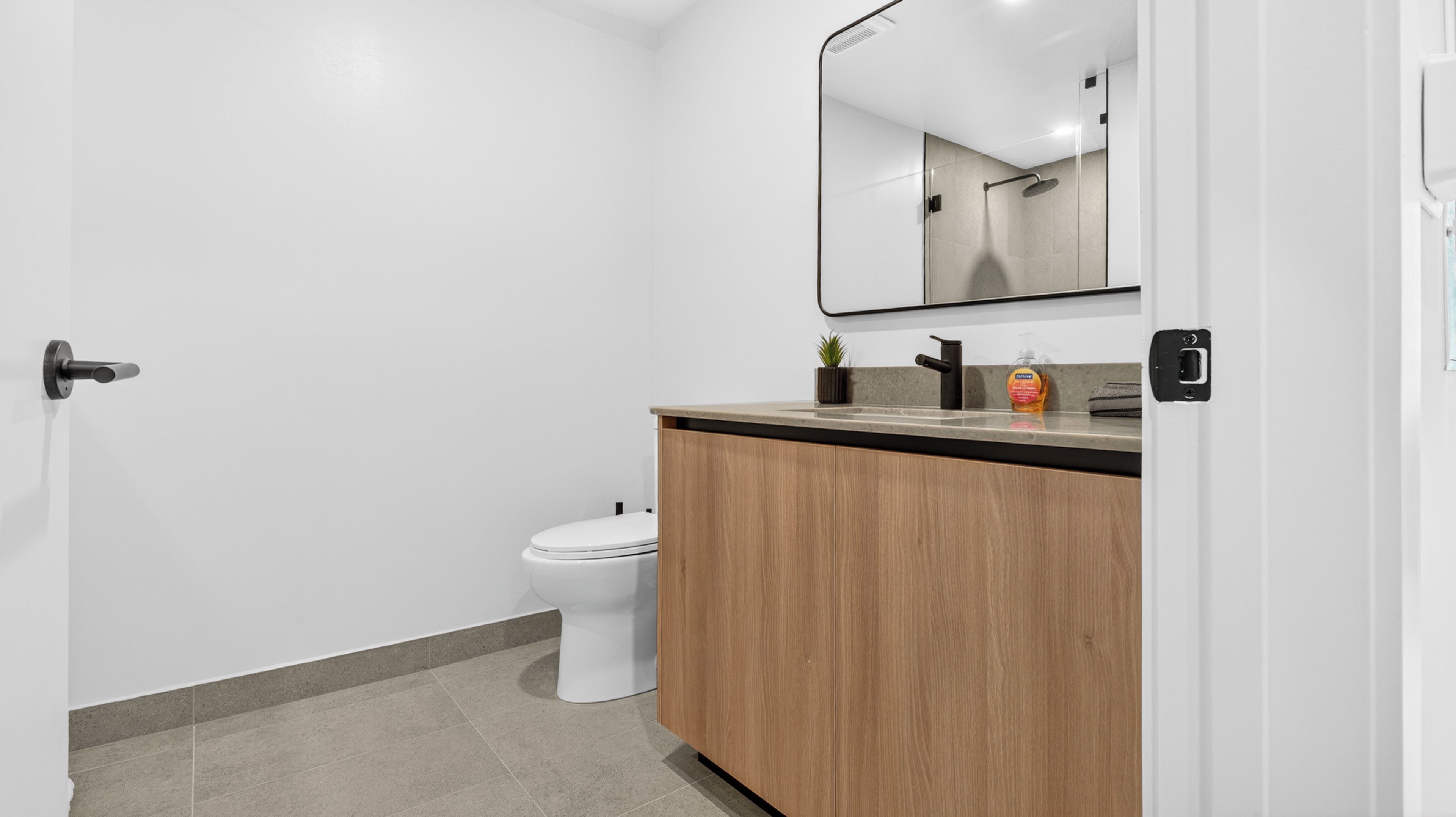 Un baño moderno con inodoro, tocador de madera y espejo.