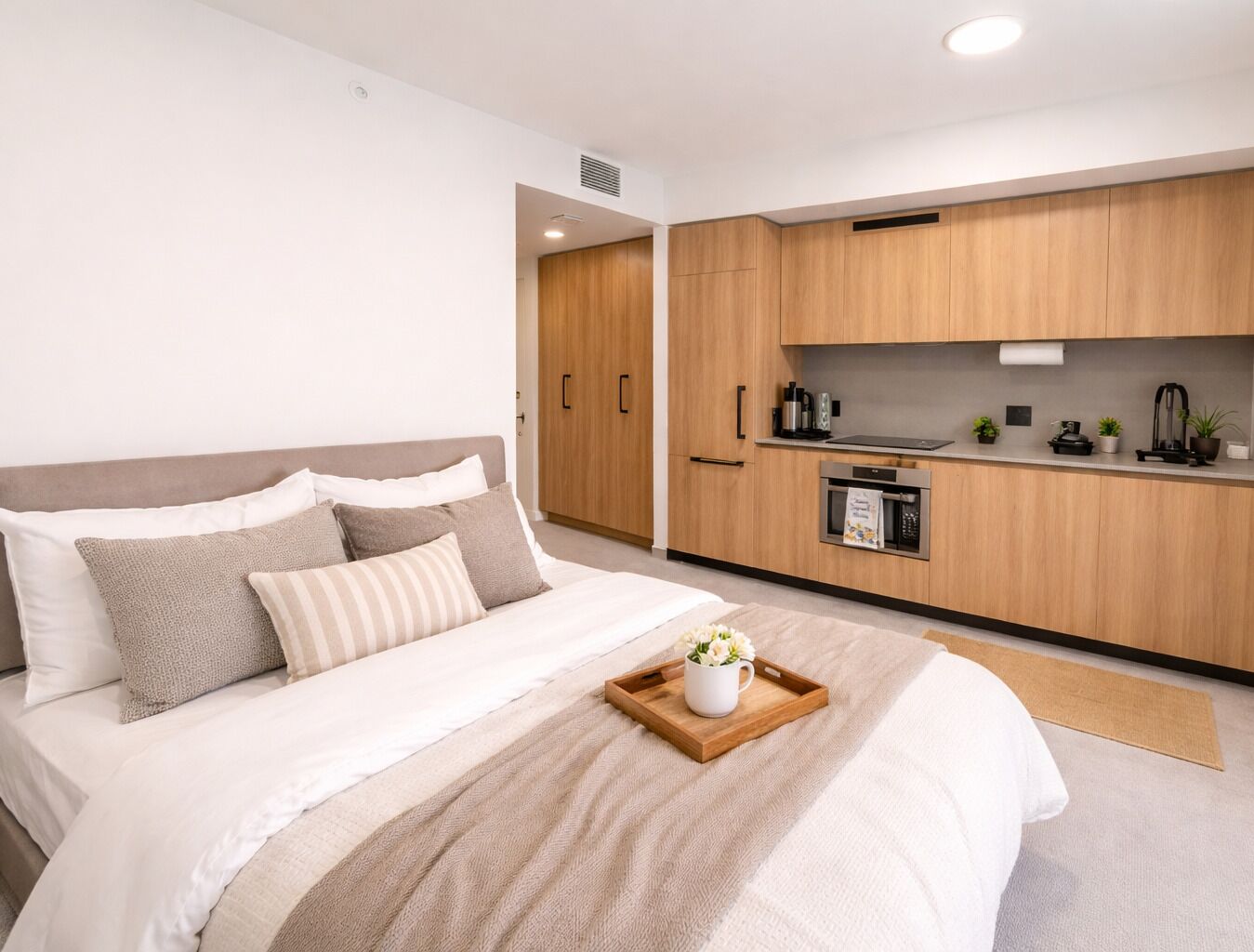 Un dormitorio moderno con una cama grande, un armario de madera, una kitchenette y un baño pequeño.