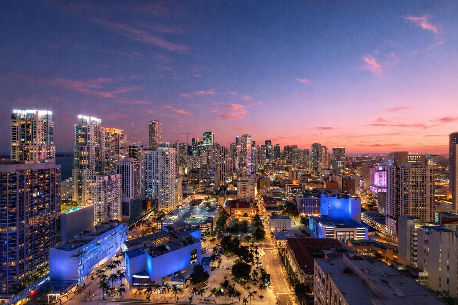 A cityscape at dusk with high-rise buildings, a central plaza, and illuminated structures.