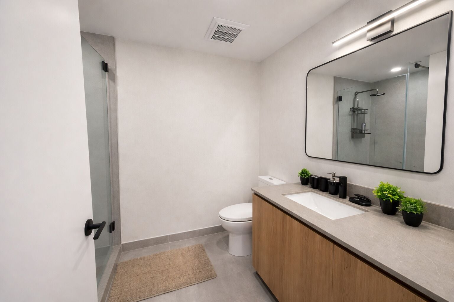 A modern bathroom with a toilet, sink, mirror, and shower.