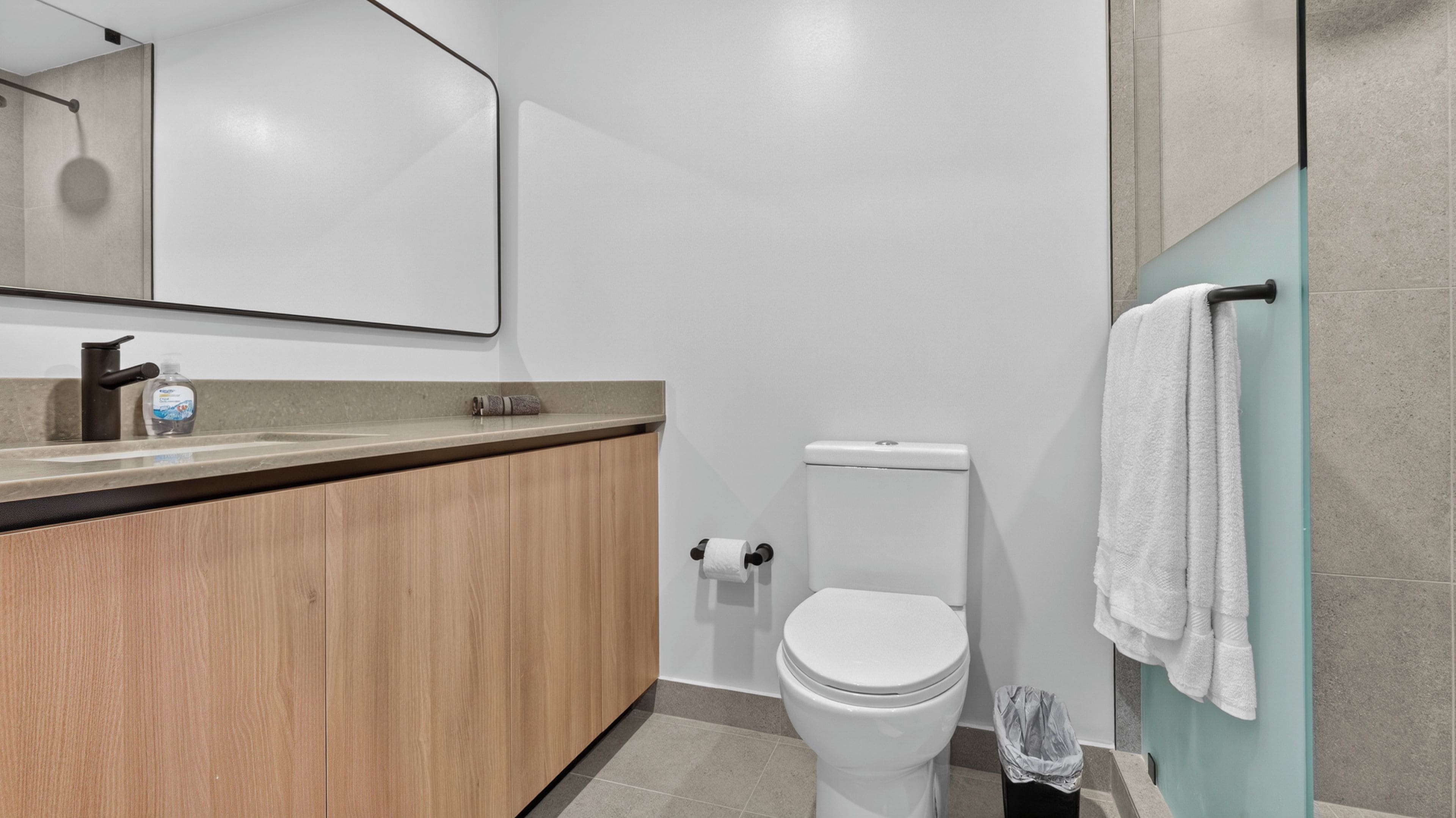 Un baño moderno con tocador de madera, inodoro, cabina de ducha de vidrio y perchero para toallas.