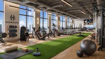 A gym with exercise equipment, a green artificial turf, and a city view.