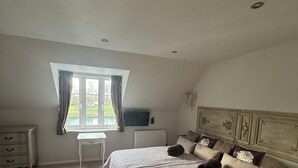 A bedroom with a large bed, a desk, and a window with curtains. - Spacious Lakeside Family Lodge in the Cotswolds | Sleeps 6 | Private Deck (Cirencester)