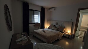 Ein Schlafzimmer mit Bett, Nachttisch, Lampe und einem Fenster mit Vorhängen.