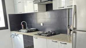 Eine moderne Küche mit weißen Schränken, einem Edelstahlkühlschrank, einem Gasherd und einer schwarzen Küchenzeile.
