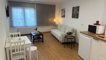 A compact living space with a kitchenette, a dining area, a sofa, and a window with blinds.