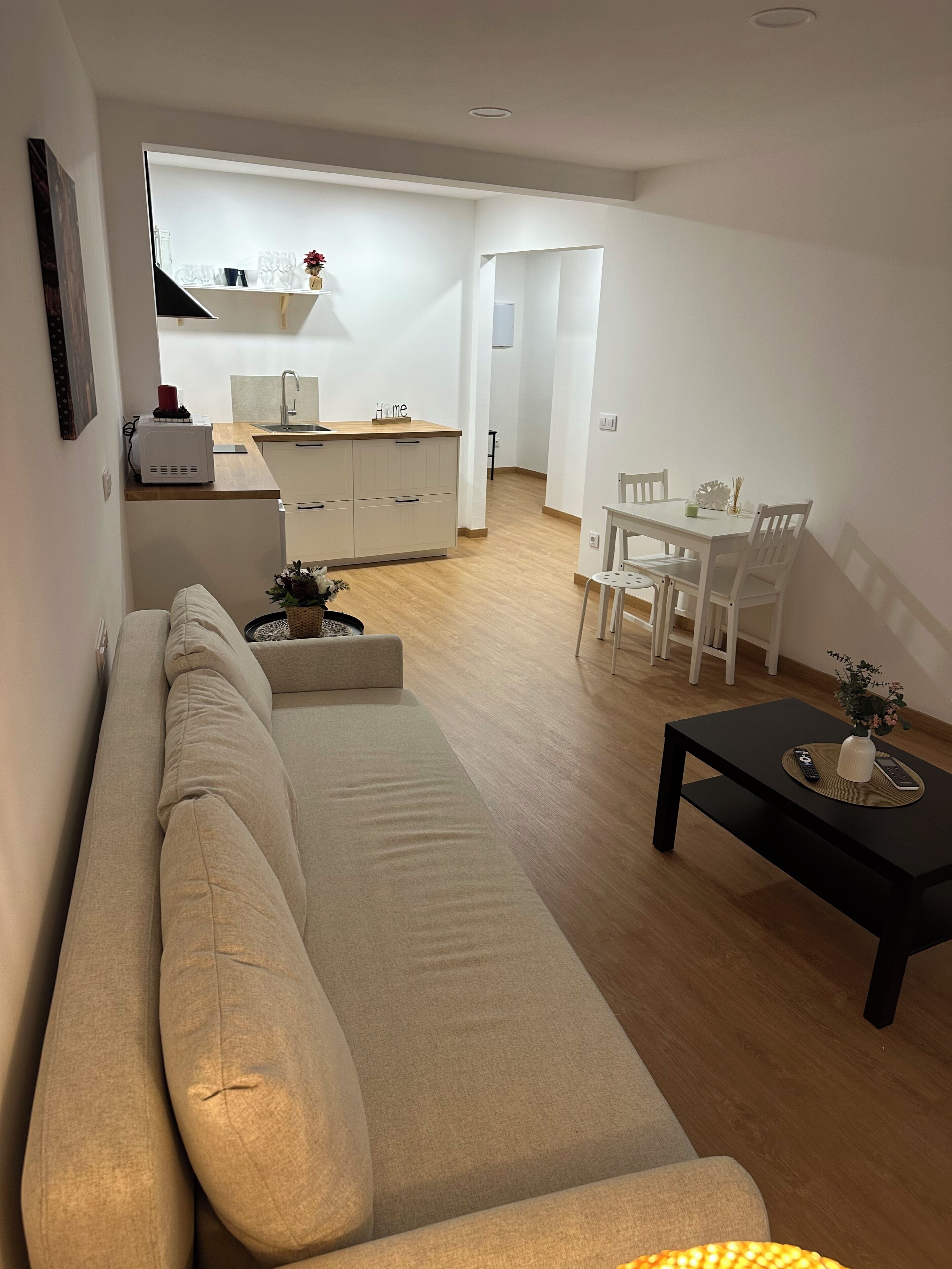 Een moderne woonkamer met een bank, een eettafel met stoelen, een keukenhoek en een gang.