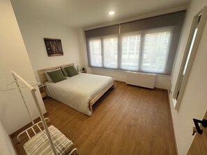 Un dormitorio con cama, ventana con cortinas, radiador y mesita de noche.