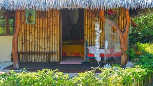 Une hutte en bambou avec un lit à l’intérieur, entourée de verdure.