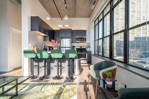 A modern kitchen with a bar area, large windows, and a view of the city. -  McCormick Suites by Slumber Stay (Chicago)