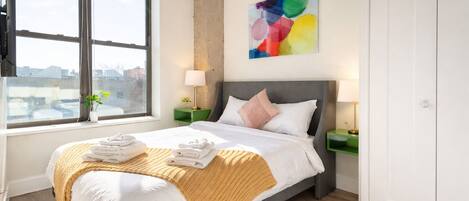 A hotel room with a bed, a window, a painting, and a green rug.