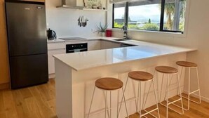 A modern kitchen with a central island, bar stools, a refrigerator, and a window with a view.