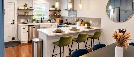 A modern kitchen with a central island, stainless steel appliances, and a dining area with a dark wood table and green chairs.