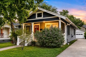 A two-story house with a front porch, a garage, and a well-maintained lawn. - Honky Tonk Heights | 2 Kings, Fire Pit, EV Charger (Houston)