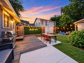 A backyard with a barbecue grill, a wooden deck, and a seating area with chairs and a table. - Honky Tonk Heights | 2 Kings, Fire Pit, EV Charger (Houston)