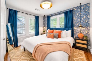 Ein Schlafzimmer mit einem großen Bett, blauen Vorhängen, Wandtapete mit Muster und einer Deckenleuchte.