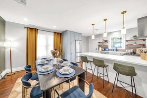 Une cuisine moderne avec des meubles blancs, un îlot central, des tabourets de bar et des luminaires suspendus.