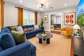 A modern living room with a blue sofa, a yellow armchair, and a round coffee table. - Honky Tonk Heights | 2 Kings, Fire Pit, EV Charger (Houston)