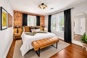 A bedroom with a bed, a bench, a nightstand, a lamp, a mirror, and a window with curtains. - Honky Tonk Heights | 2 Kings, Fire Pit, EV Charger (Houston)