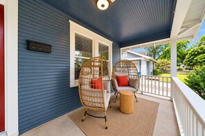 A porch with two wicker chairs, a small round table, and a blue exterior wall. - Honky Tonk Heights | 2 Kings, Fire Pit, EV Charger (Houston)