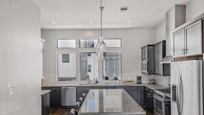 A modern kitchen with a central island, stainless steel appliances, and a large window with blinds. - Houston Townhome w/ Skyline Views & Rooftop Patio (Houston)