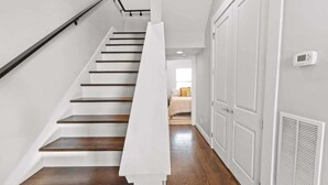 A staircase with wooden steps and white walls, leading to a room with a bed and a window. - Houston Townhome w/ Skyline Views & Rooftop Patio (Houston)