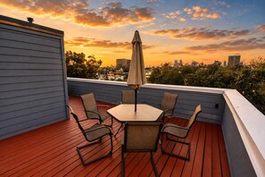 A rooftop patio with a table and chairs, an umbrella, and a cityscape view at sunset.