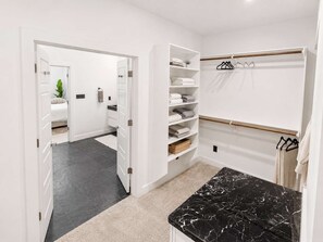 A modern bathroom with a black marble countertop, white storage shelves, and a walk-in closet with hanging clothes. - Montrose Rooftop Townhome | 3 Suites, Sleeps 8 (Houston)