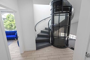 Un interior moderno con una escalera espiral, un sofá azul y vistas al exterior con vegetación.