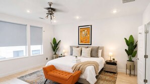 A bedroom with a bed, a nightstand, a floor lamp, a window with blinds, and a ceiling fan. - Montrose Rooftop Townhome | 3 Suites, Sleeps 8 (Houston)