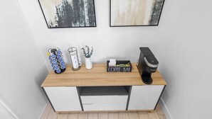 A kitchenette with a coffee maker, a coffee bar sign, a plant, and a mug on a wooden countertop.