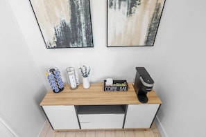 Una kitchenette con cafetera, un letrero que dice 'Coffee Bar', una planta y una taza sobre una encimera de madera.