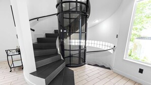A modern spiral staircase with a glass railing, leading to a landing.